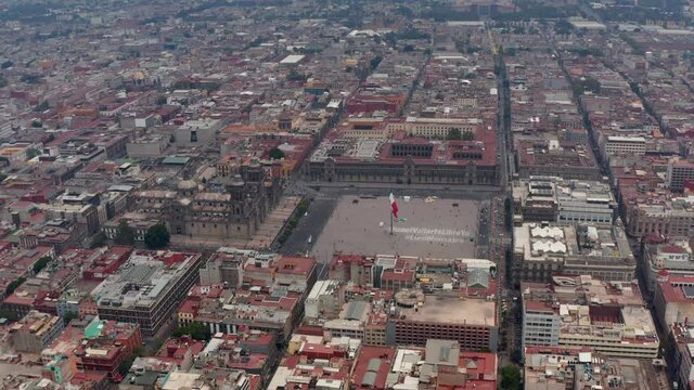 Forwards reveal of Catedral Metropolitana de la Ciudad de Mexico and Plaza de la Constitucion with large state flag. Aerial footage of historic city centre. Mexico City, Mexico.