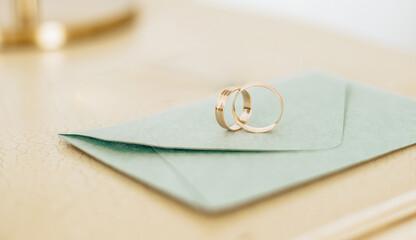Two wedding rings lie on an invitation with gold background