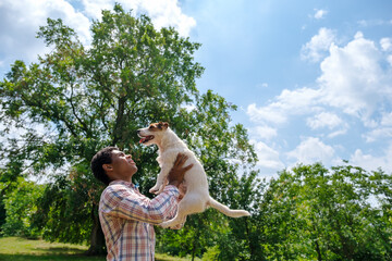 Afican American man throws Jack Russell dog outdoors in park in summer