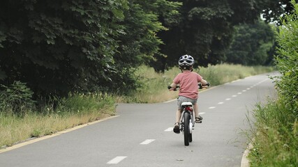 Child riding bicycle on the bike path at rain. Kid in helmet learning to ride at summer. Happy boy riding bike, having fun outdoors on nature.