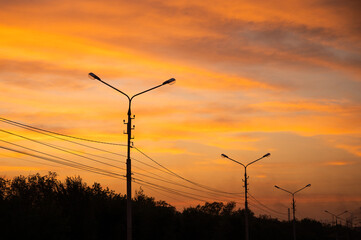 Fototapeta na wymiar Electric poles with lanterns against vivid sunset sky