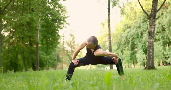 Young man doing yoga pose ina park at morning. Guy doing stretching. Slow motion