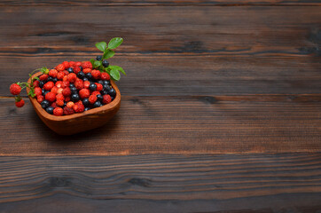 forest berries in a bowl on a wooden background , copy space