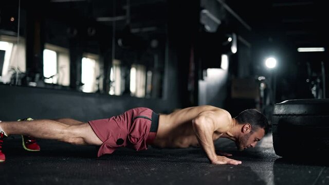 A handsome young muscular sportsman is doing exercise. A trainer performing push ups in the gym. Crossfit training. Concept of lifestyle fitness health and sports. Maximum focus and strength.