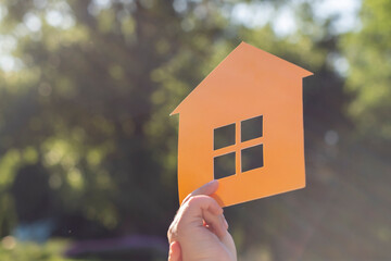Paper mock-up stencil of the house, which is held by the hand of a child, in the rays of the sun...