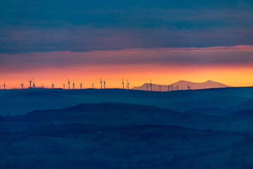 sunset in the mountains with wind turbine silhouettes