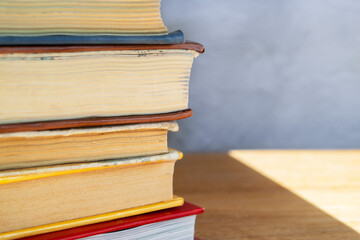 Stack of colorful hardback books on wooden table close up against gray and blue concrete wall