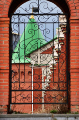 Iron koala gate with a cross behind which is a red brick wall. Russia Yoshkar-Ola 01.05.2021. High quality photo