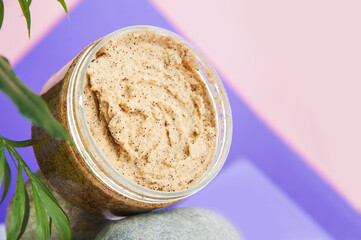 Coffee scrub in plastic jar on texture stone and copy space. Homemade cosmetics, skincare products on natural podium on pink background. Top view.
