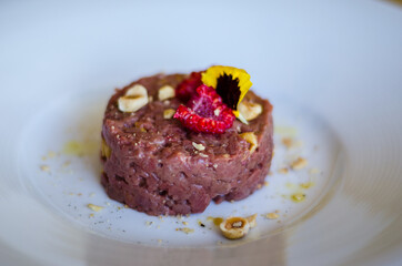 raw meat tartare macro with raspberry and nuts on white plate