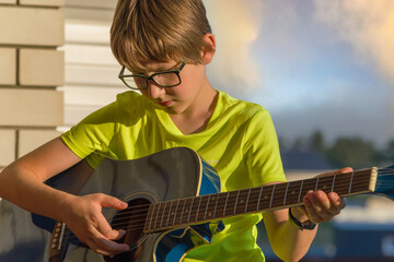 Boy sitting and playing semi-acoustic blue guitar at sunset