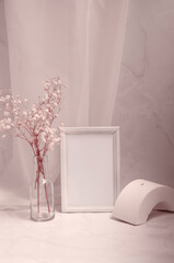 Modern interior still life with geometric white shape, picture frame with paper sheet, gypsophila flowers in the glass bottle. Pastel colors background, minimalist design mock up.