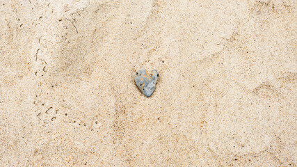 Heart-shaped gray sea rock on sandy beach