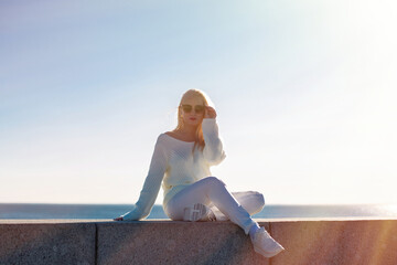 Fototapeta na wymiar Young beautiful blonde woman sitting near the sea on the beach at sunrise time