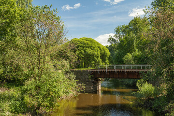 Fototapeta na wymiar Small railway bridge over a small river in a summer forest among greenery