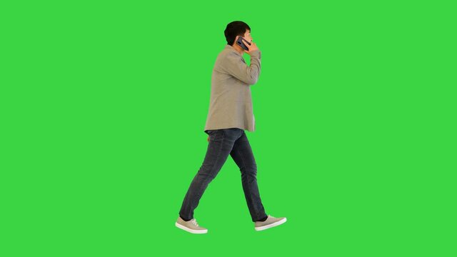 Young asian man walks talking on his smartphone and smiling on a Green Screen, Chroma Key.