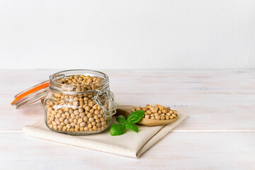 Raw chickpea beans in a clip top glass jar and in a large wooden spoon on a white rustic table. Dry...