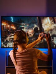 Youth culture, video games. A woman is sitting in a room with a joystick in her hand. In front of her is a large personal computer monitor. There is neon light in the room. Rest time, hobby.