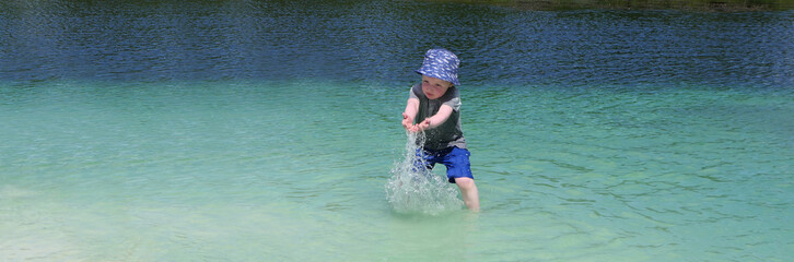 Small boy with a blue sun hat playing on a fresh water sandy beach in Vacation resort in Ireland