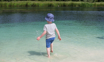 Small boy with a blue sun hat playing on a fresh water sandy beach in Vacation resort in Ireland