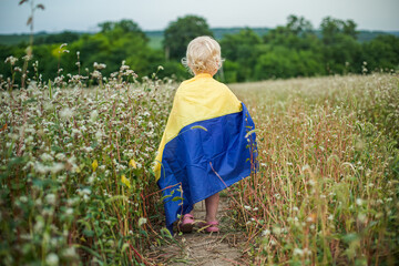 Wrapped in blue yellow flag, girl leaves. child with symbol of Ukraine. AUkrainian woman walks on...