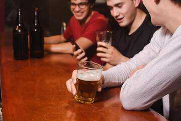 Detail of drunken friends laughing while drinking beer at the bar.