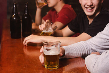 Detail of happy friends drinking beer while laughing at the bar.
