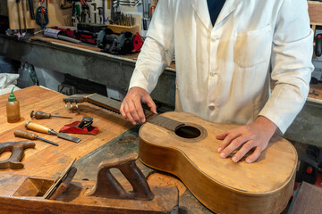 LUTHIER IN THE WORKSHOP WITH TOOLS RESTORING A SPANISH OR CLASSICAL GUITAR. CRAFTSMAN CONCEPT.