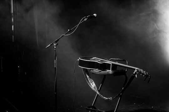 Microphone, guitar and stool on a concert stage. Black and white high contrast with spotlight and smoke. Live singing performance. Music show background. Spotlight smoke empty stage.