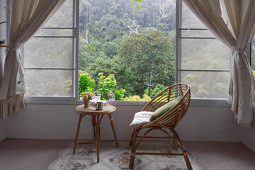 Cozy room with chair and table with book and coffee cup, big window and curtain on green mountain view background.