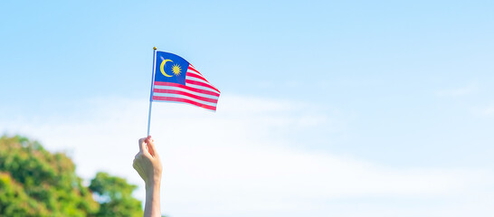 hand holding Malaysia flag on blue sky background. September Malaysia national day and August...