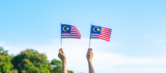 hand holding Malaysia flag on blue sky background. September Malaysia national day and August...