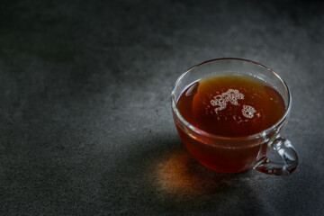 A cup of hot, black tea in a glass cup on a gray ceramic countertop.