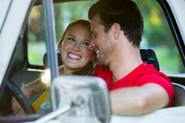 Young couple sitting in vintage pick up truck , guy with his arm around the girl while she looks over at him smiling. 