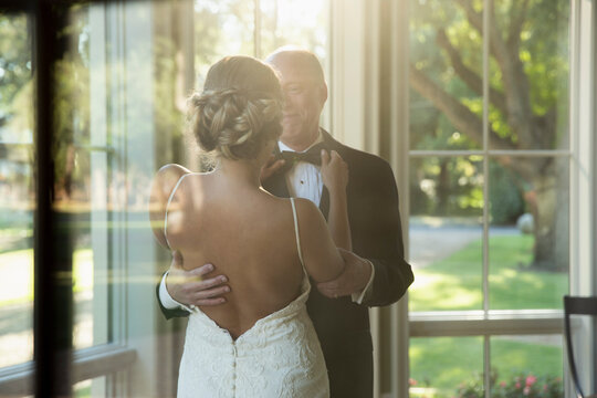 Bride fixing her fathers bow tie, seen through window