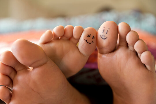 Close-up of bare feet sticking out from covers while couple lays in bed, with smiley faces drawn on big toes