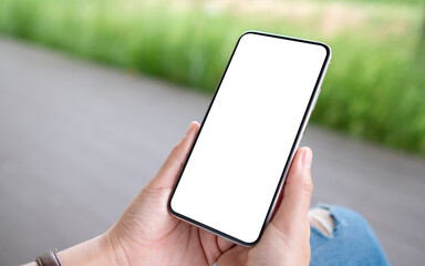 Mockup image of a woman holding mobile phone with blank white desktop screen in the outdoors