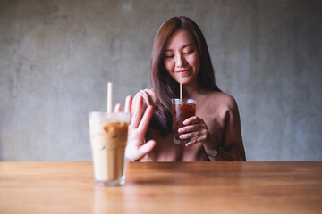 A beautiful young woman choosing to drink black coffee and making hand sign to refuse sweetened milk coffee