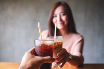 A woman and a man clinking coffee glasses together in cafe