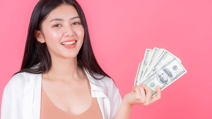 Successful beautiful Asian business young woman holding money US dollar bills in hand on pink background , business concept