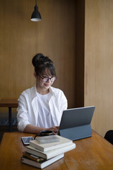 Young Asian woman sitting in library and using computer tablet.