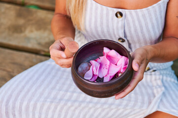 Woman hands with tibetan singing bowl with rose petals inside. S