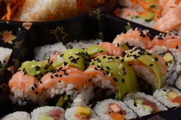 Set of sushi rolls  on a black plastic platter decorated with soy sauce and spices. Ready for delivery
