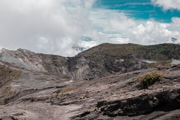 view of the main crater surrounded with little vegetation rocky and sandy terrain with blue sky in the Irazu Volcano National Park - Cartago - Costa Rica - Central America