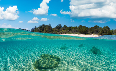 Fototapeta na wymiar Split-shot, over-under shot. Half underwater half sky with a turquoise water and a white sand beach in the distance during a sunny day. Liscia Ruja, Sardinia, Italy. 