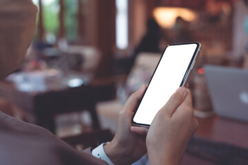 Cell phone mockup image blank white screen.  Woman hand holding, using mobile phone in coffee shop, close up