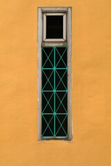 Glass windows with ventilation and wrought iron to prevent thieves on the walls of an old building painted in classic yellow.