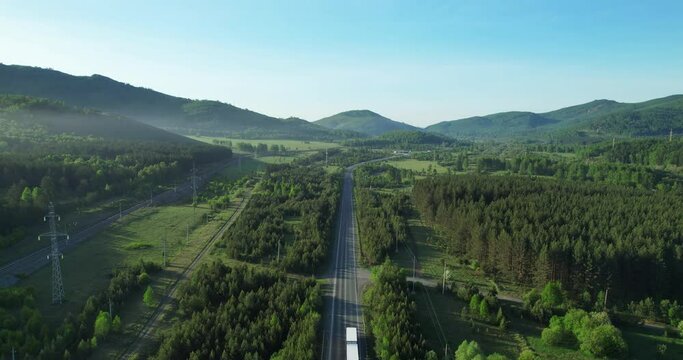 The truck goes along a picturesque road that is located among mountains and forests. The highway runs parallel to the railway.