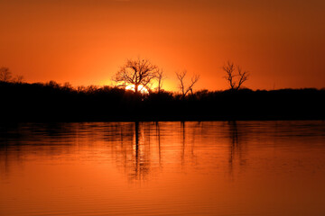 Fototapeta na wymiar Orange Autumn sunset with reflection of trees in silhouette at North Turtle Lake in Minnesota, USA 