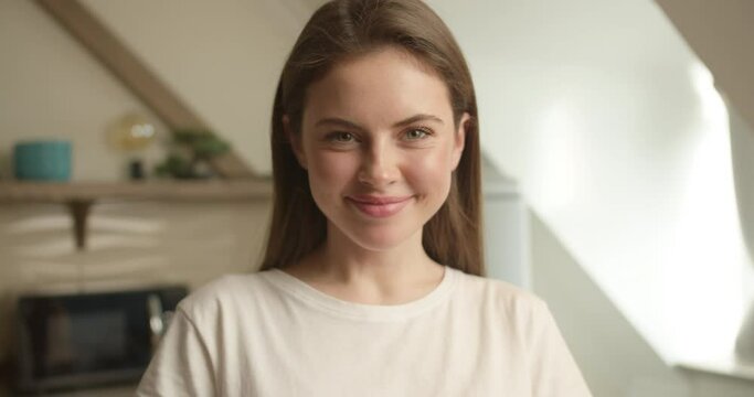 A close-up portrait of a beautiful brunette of Slavic appearance wearing a white T-shirt with loose hair that looks at the camera, curves, showing her tongue and smiling in the kitchen background